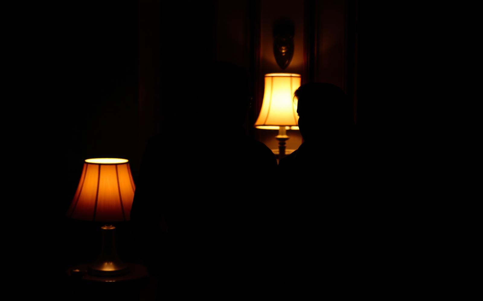 Two adults standing close in a dim lamp-lit room, faces in shadow